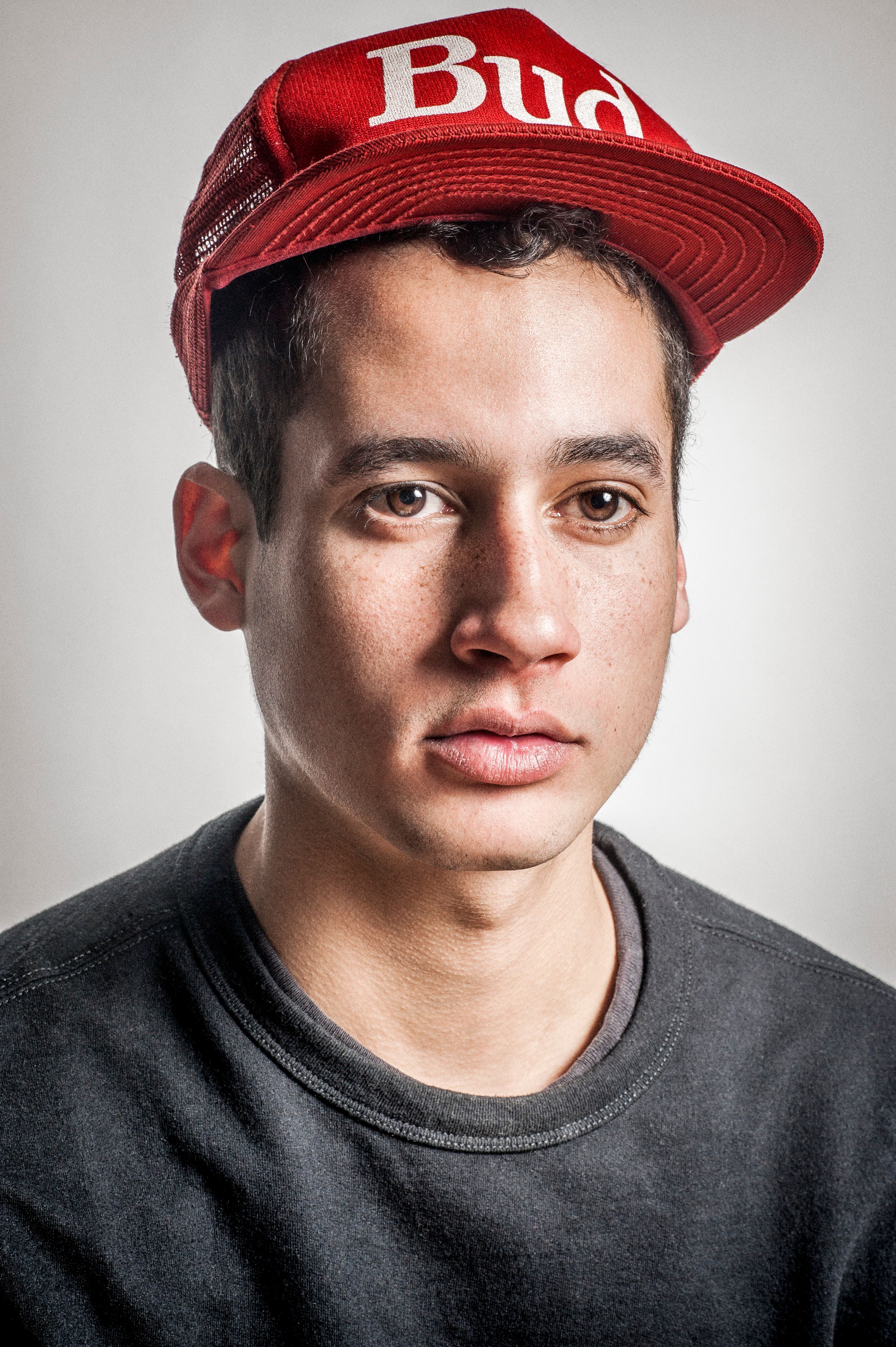 Young man with freckles wearing a red Budweiser snapback cap and black t-shirt, portrait photo.
