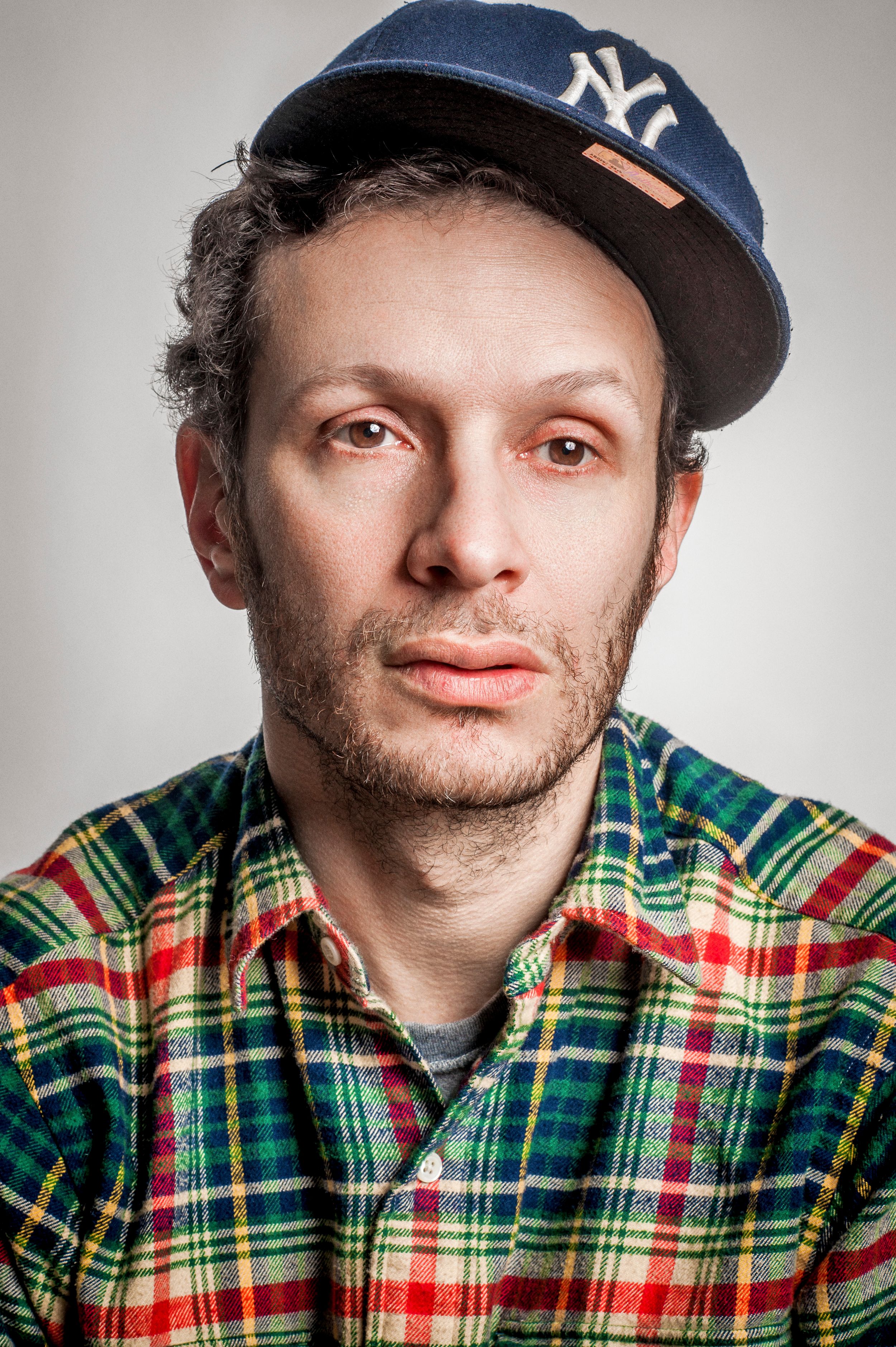 Man wearing a NY Yankees cap and plaid flannel shirt posing for a portrait photo.