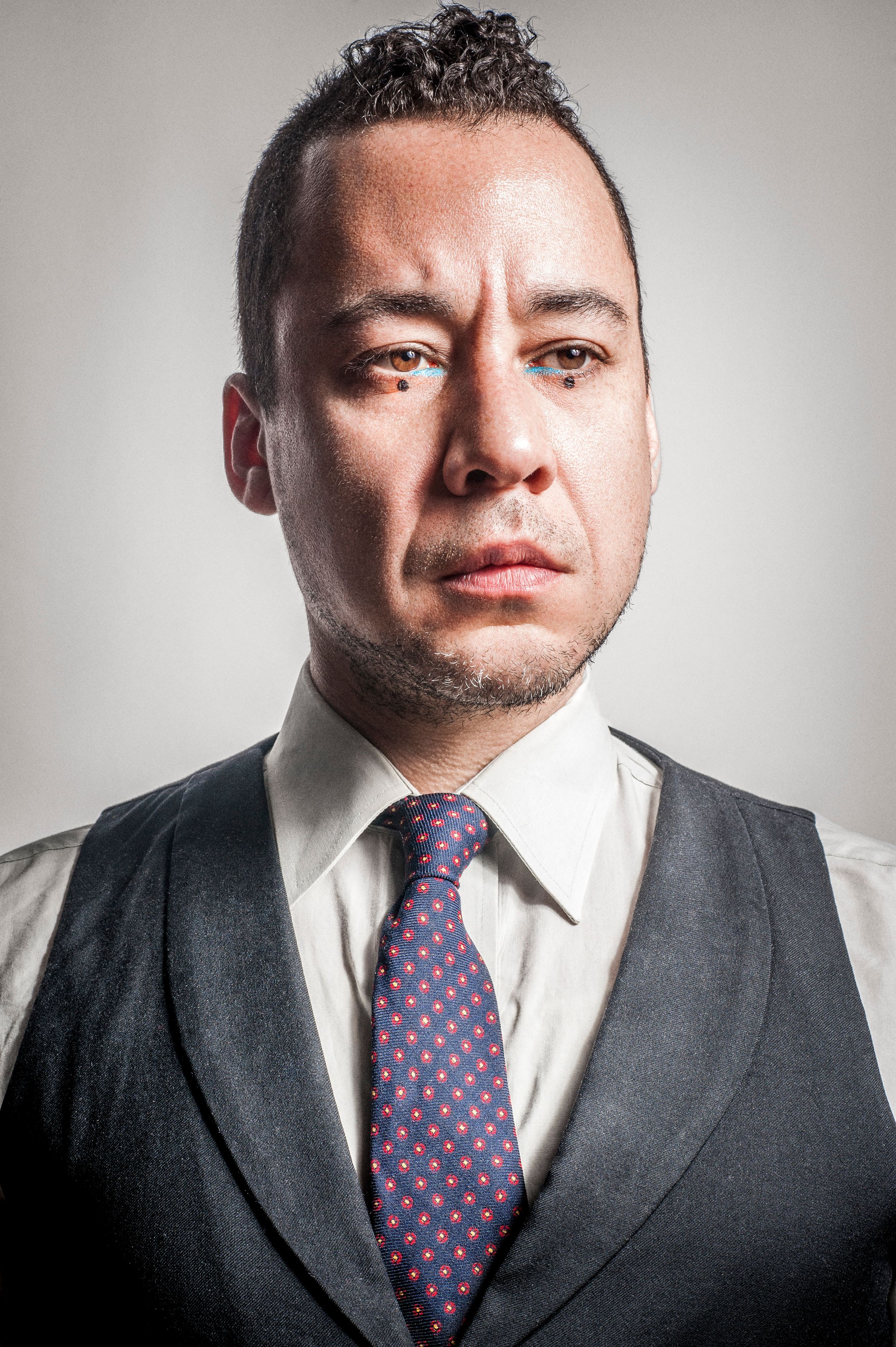 Professional man in dark vest and patterned tie posing for a formal portrait with serious expression.