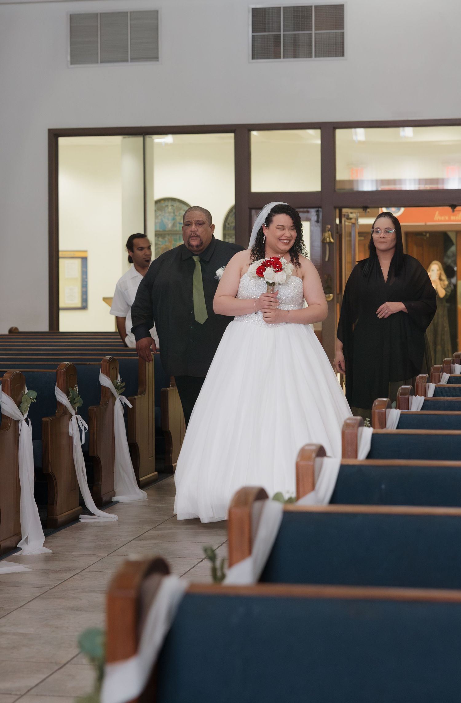 Wedding ceremony setup in a church with white pews and guests seated in formal attire.