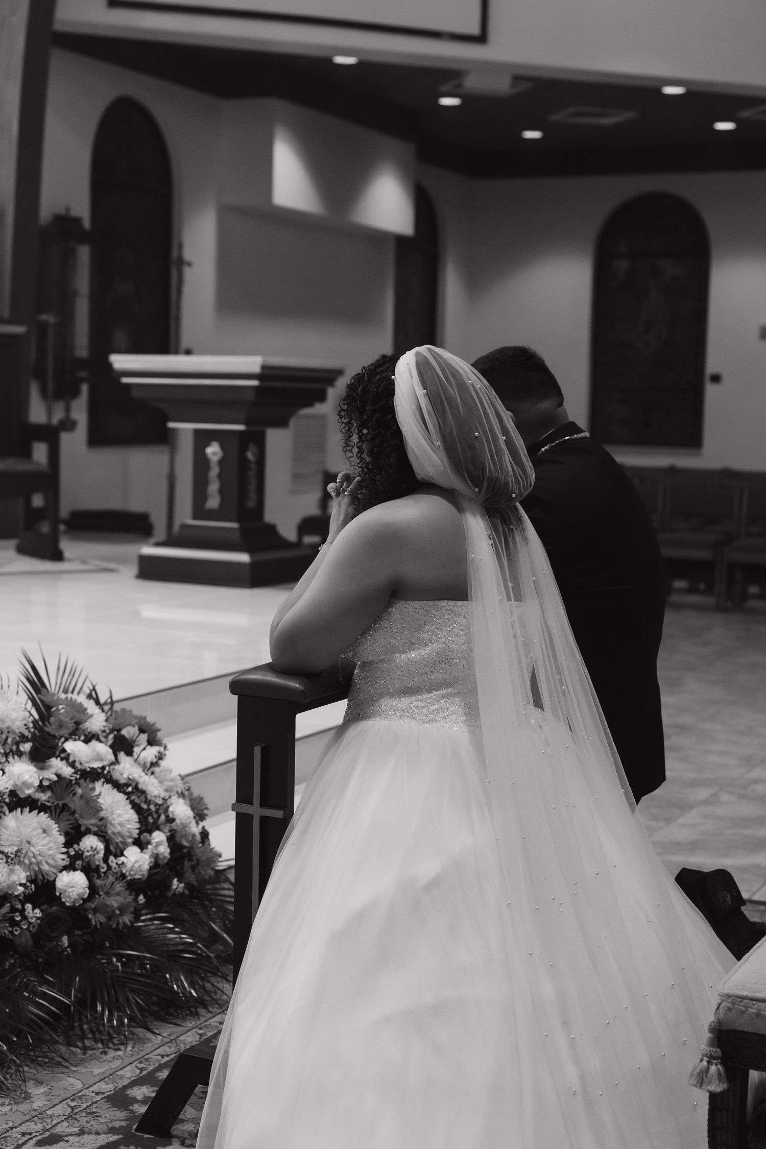 Black and white wedding ceremony photos showing the bride's dress and veil in a church setting.