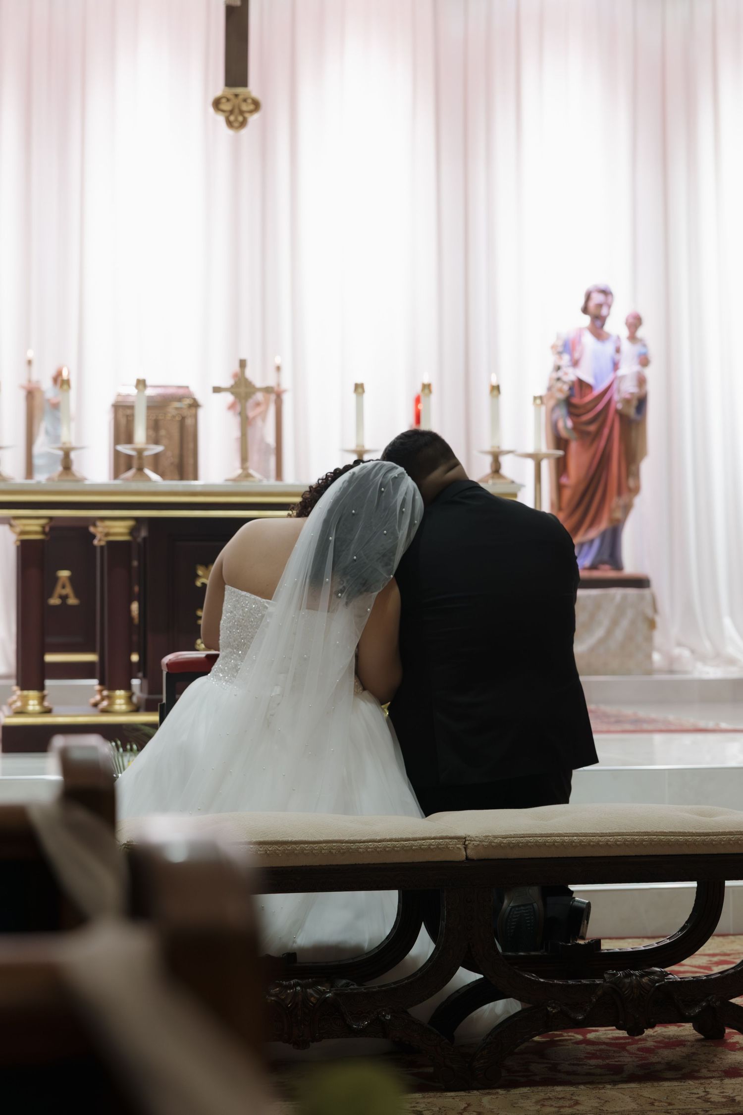 A couple in wedding attire sitting together in a church pew during their ceremony.