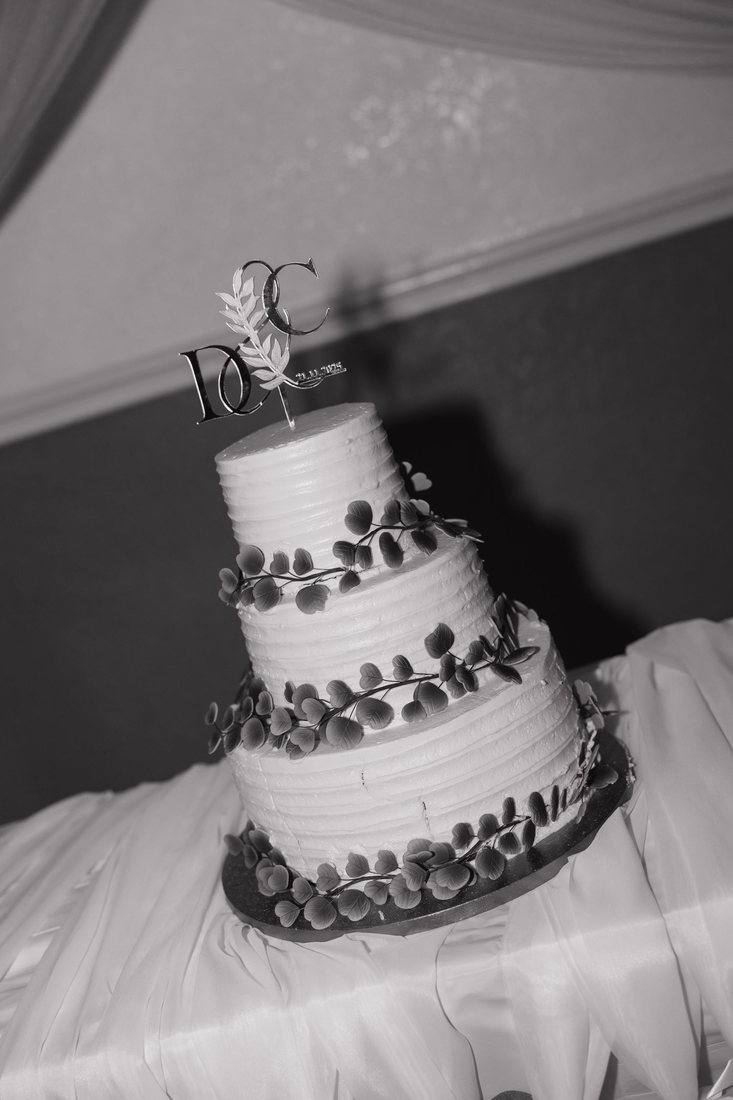 Black and white close-up shots of a white wedding cake decorated with silver leaf details.