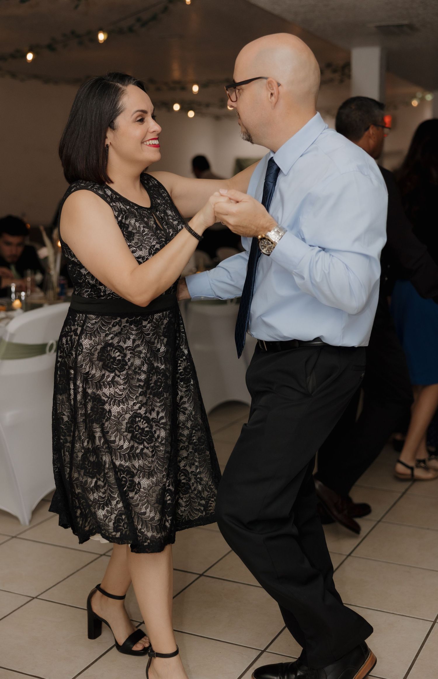 A couple dancing together at a formal event, with the woman wearing a black lace dress and the man in formal attire.
