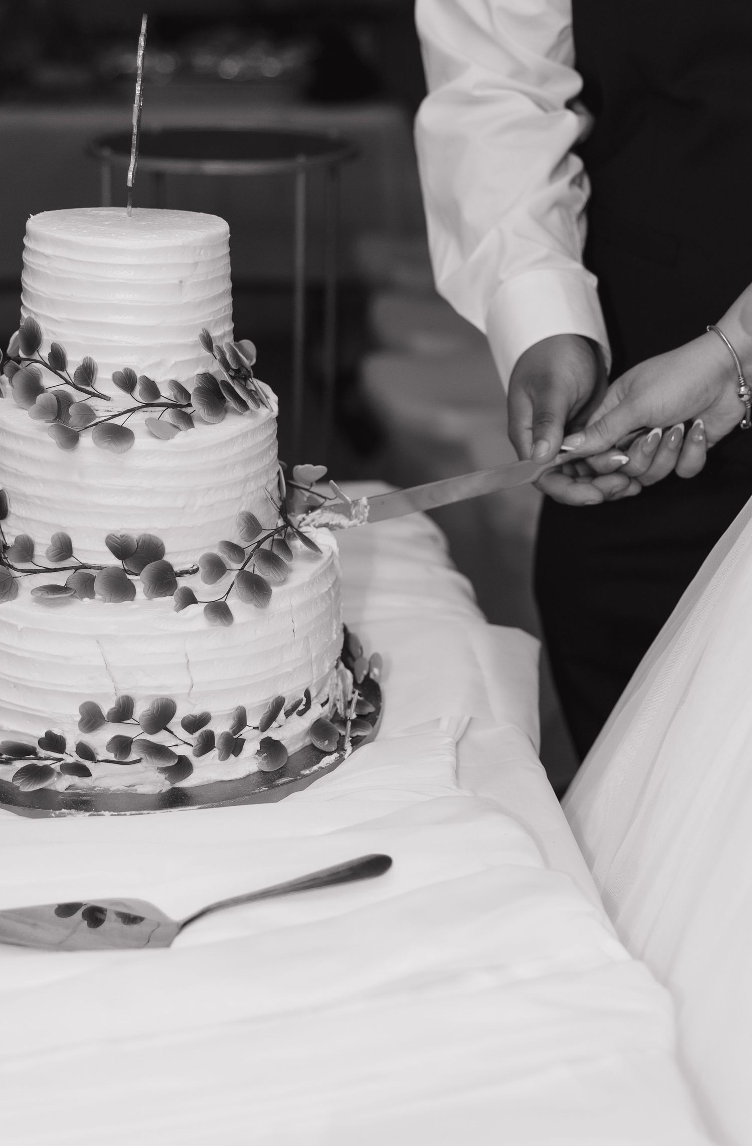 White tiered wedding cake with silver leaf decorations being cut during reception.