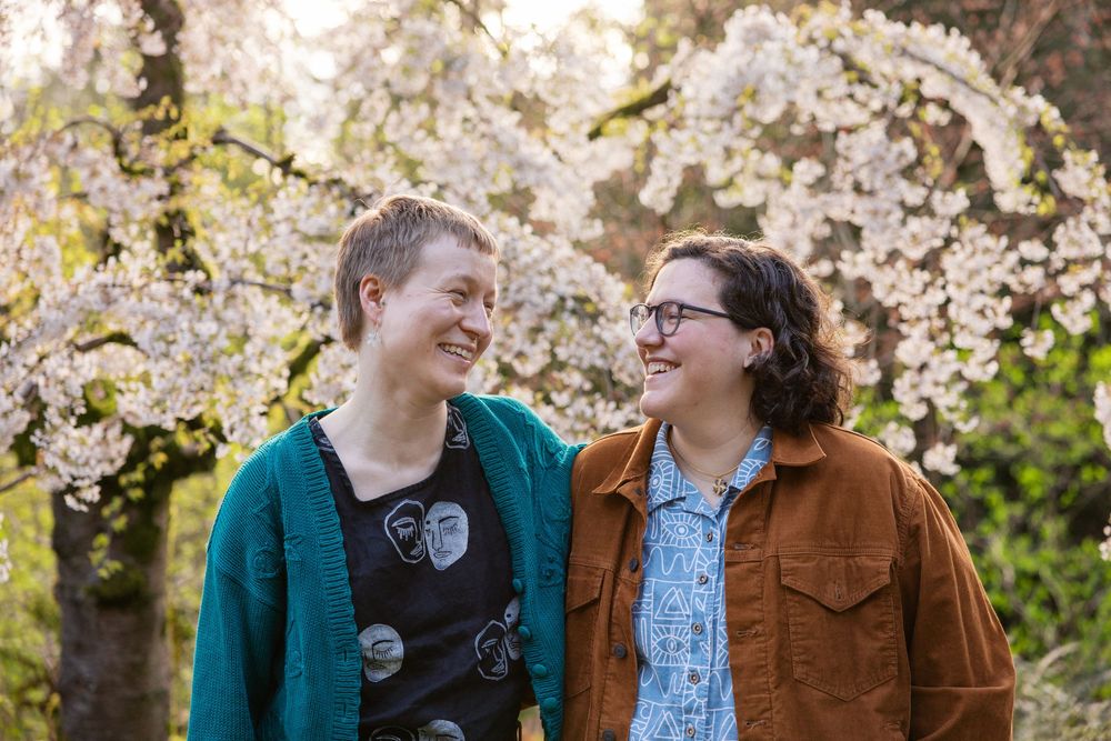 Couple laughing and gazing at each other beneath blooming white cherry blossom trees outdoors.