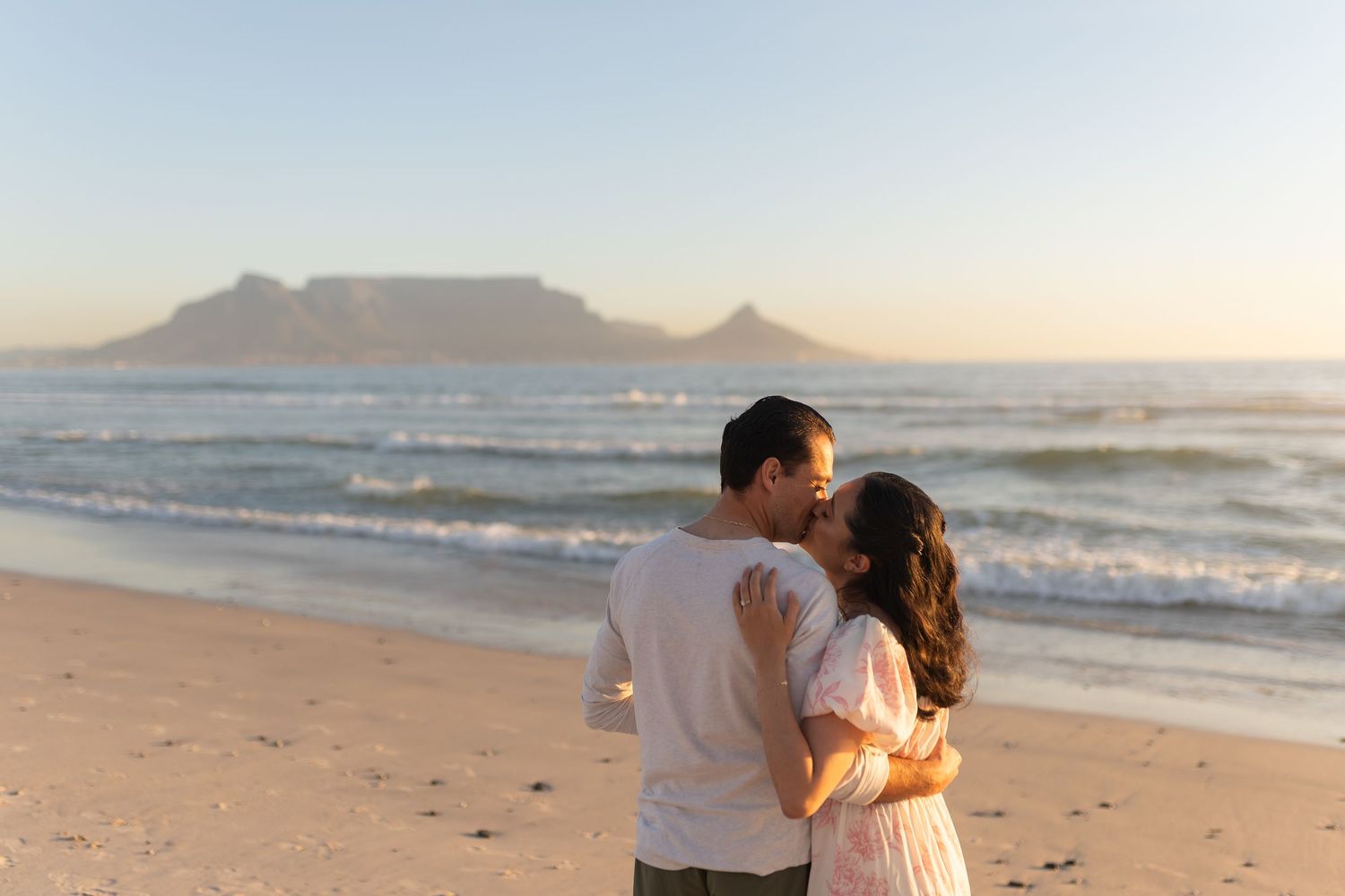 Couple sharing a romantic kiss on a beach at sunset with Table Mountain in the background in Cape Town.