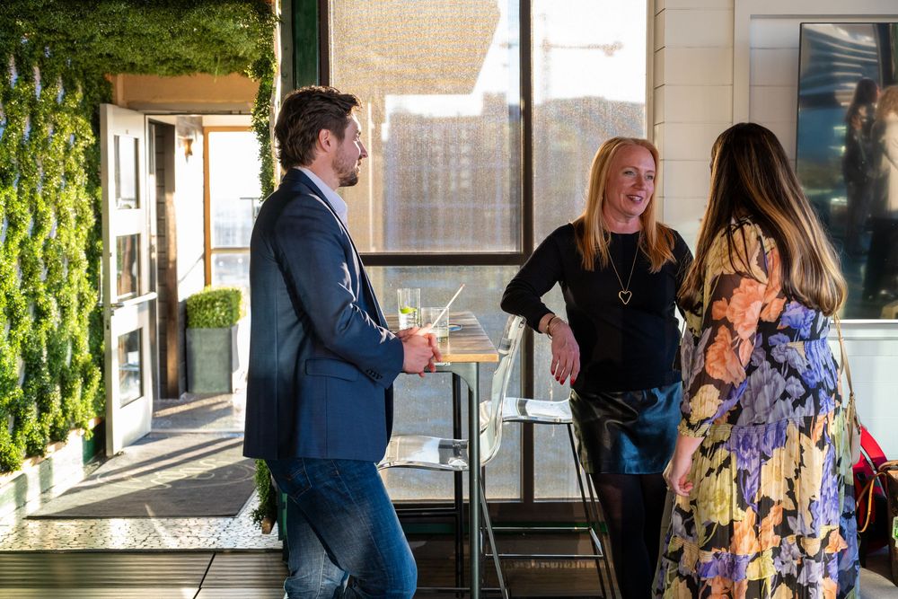 People enjoying cocktails and conversation at an upscale rooftop lounge with green wall decor.