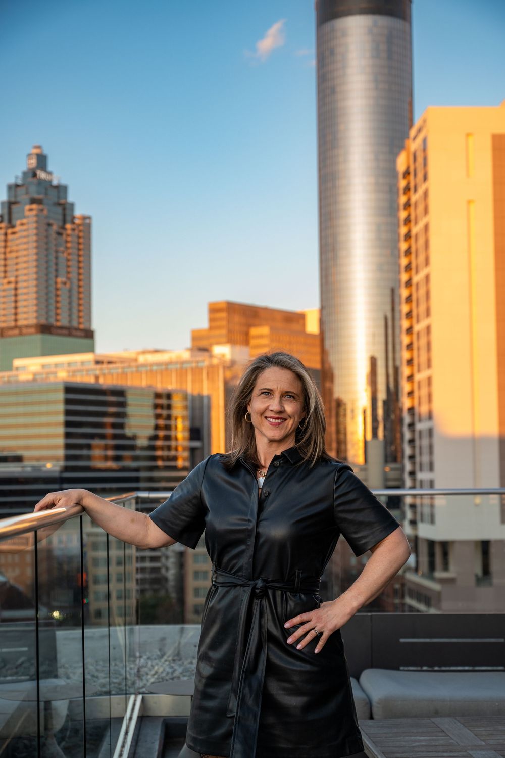 Professional portraits taken on a rooftop balcony with city buildings and golden sunset light in the background.