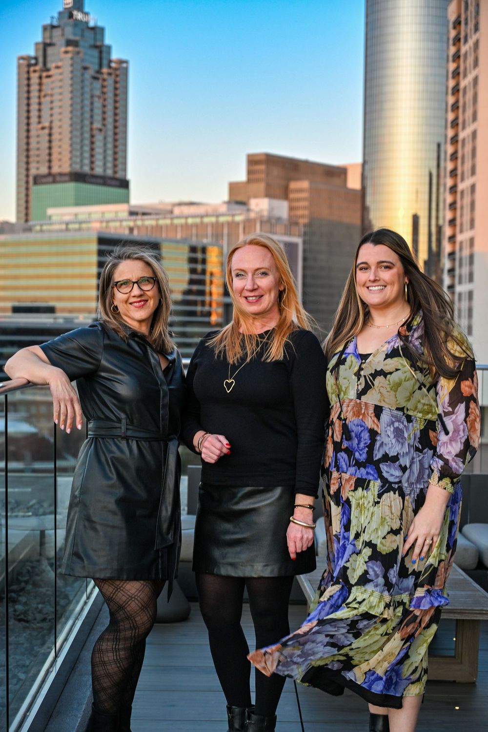 A group poses together on a rooftop terrace with city skyscrapers in the background during sunset.