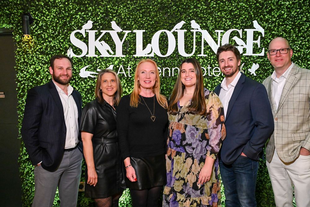 Group gathering at an event in front of a green hedge wall with Sky Lounge signage.