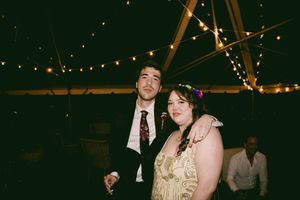 People dancing and celebrating at a wedding reception under string lights in a dimly lit venue.