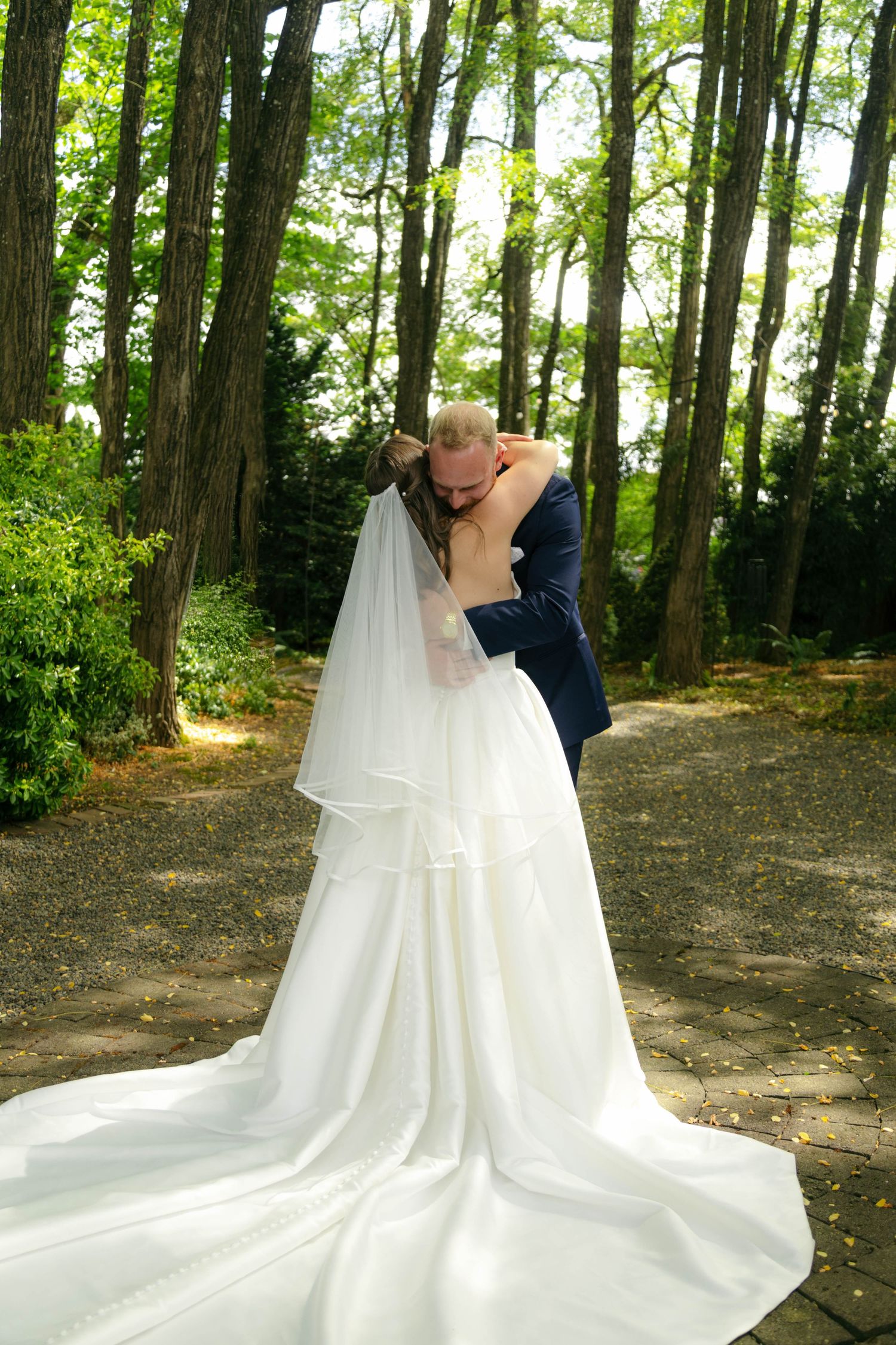 A romantic moment unfolds on a sunlit forest path beside a flowing stream on a warm summer afternoon.