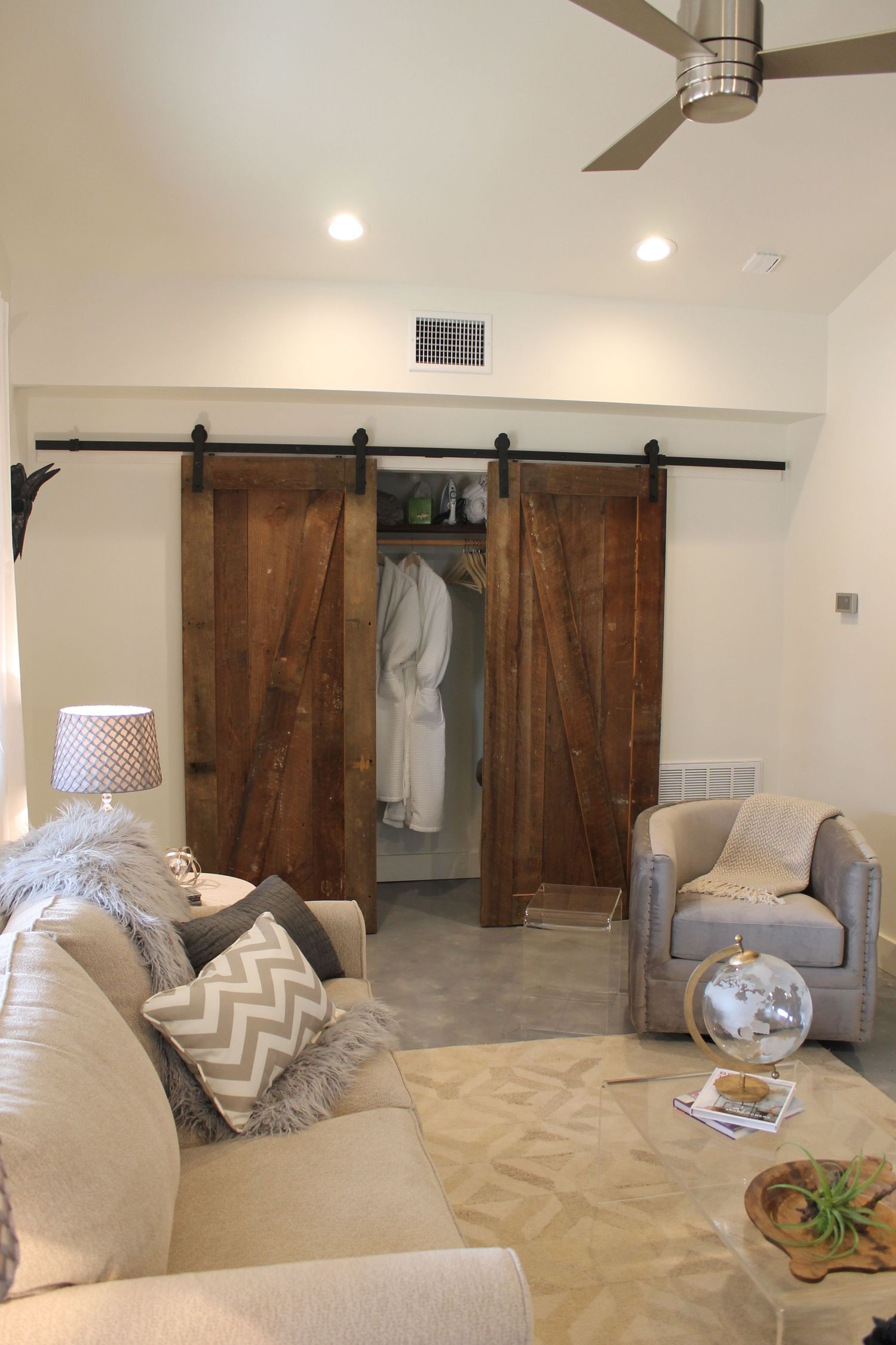 Modern living room features a grey couch, rustic barn doors, and geometric patterned carpet in neutral tones.