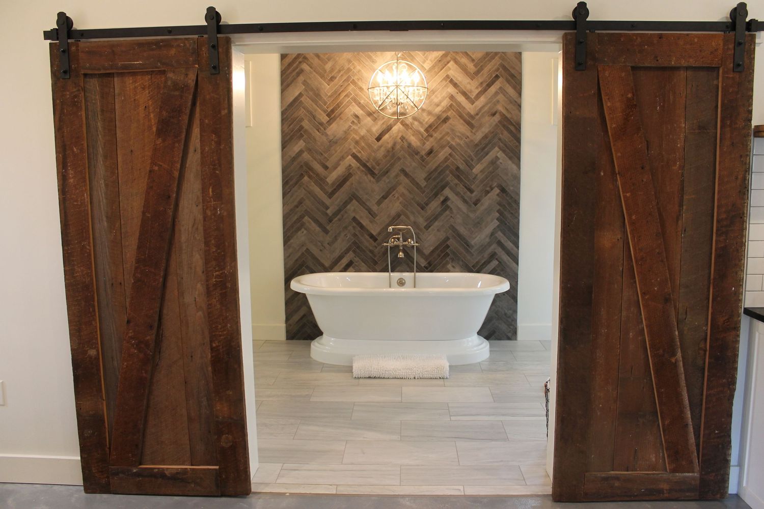 Dark brown sliding barn doors with black hardware mounted on walls featuring chevron pattern wallpaper and sconce lighting.