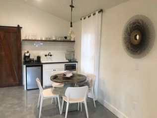 Modern minimalist kitchen and dining area with round table, white chairs, and decorative spiral wall art in neutral tones.