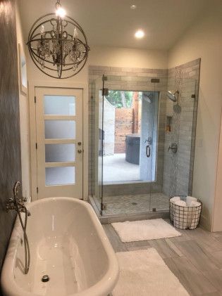 Modern master bathroom featuring marble tile, freestanding tub, glass shower enclosure and orb chandelier lighting.