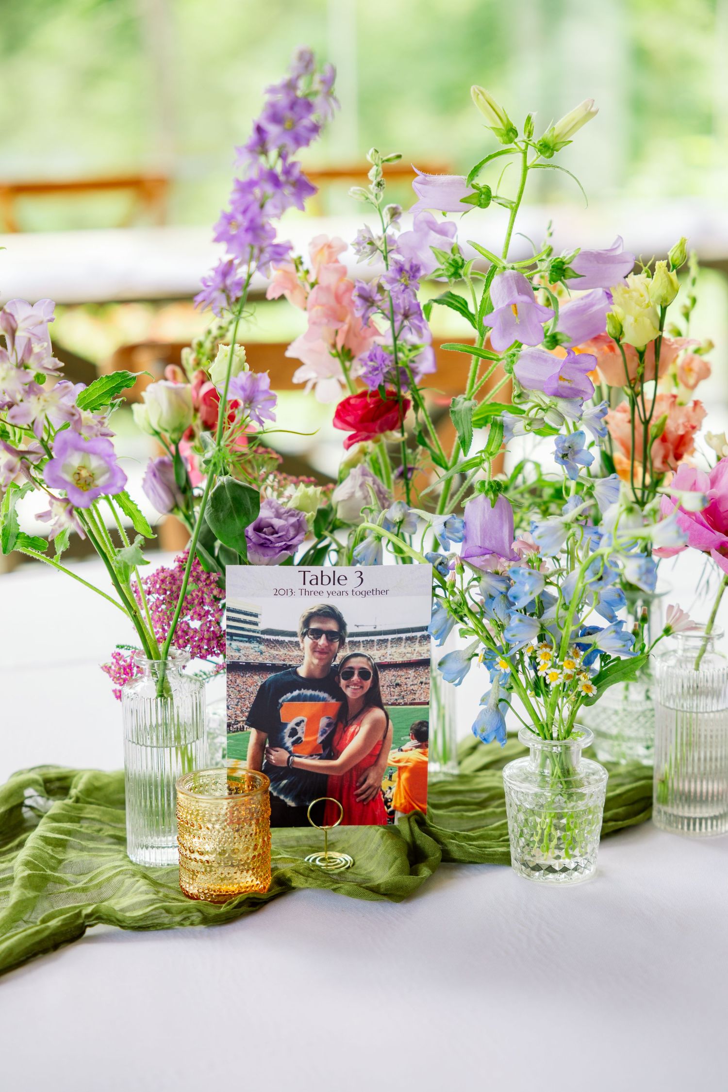 Elegant table setting with delicate purple flowers in glass vases arranged on green table runners.