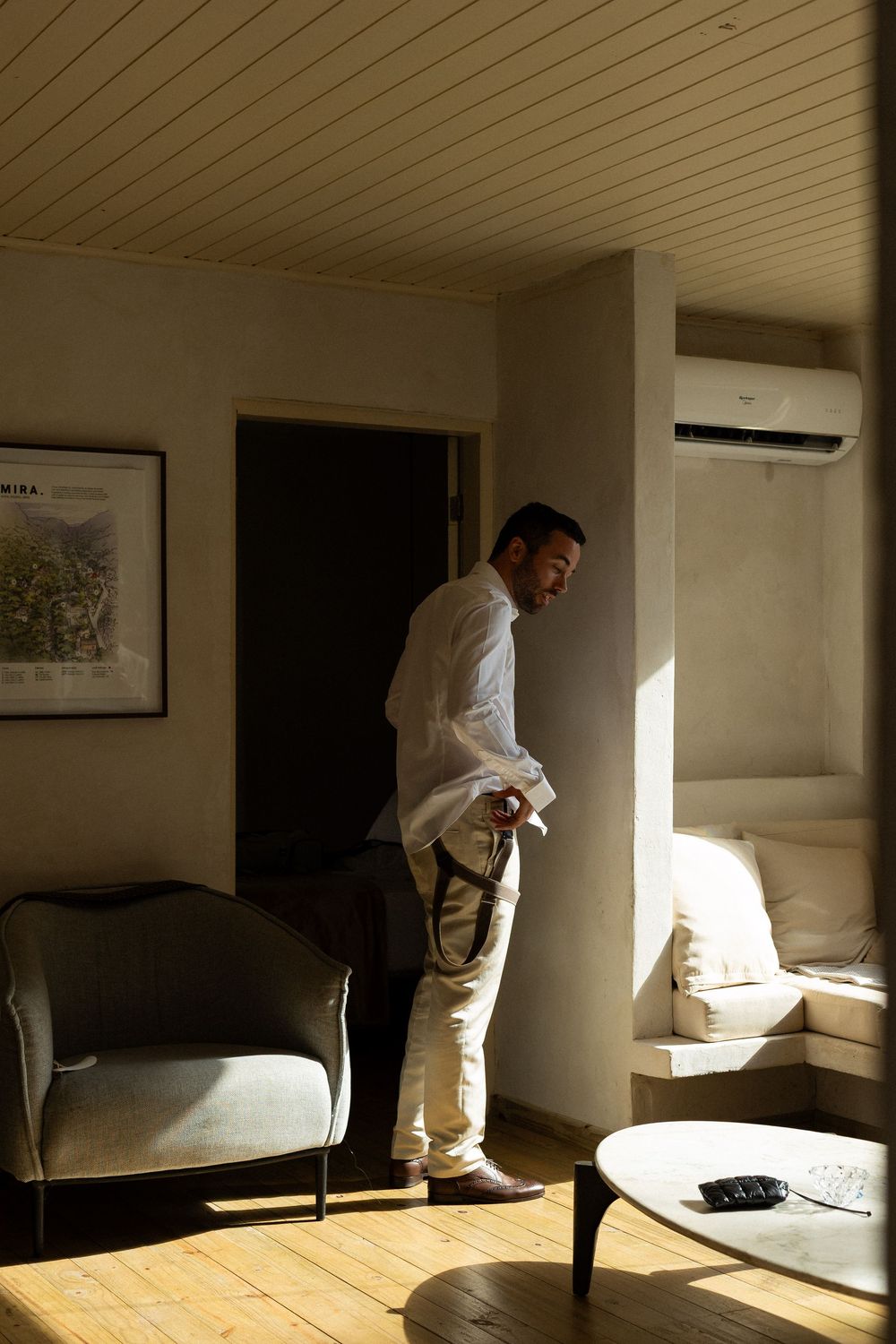 A person in a white shirt and light pants stands in a modern living room with natural light streaming in.