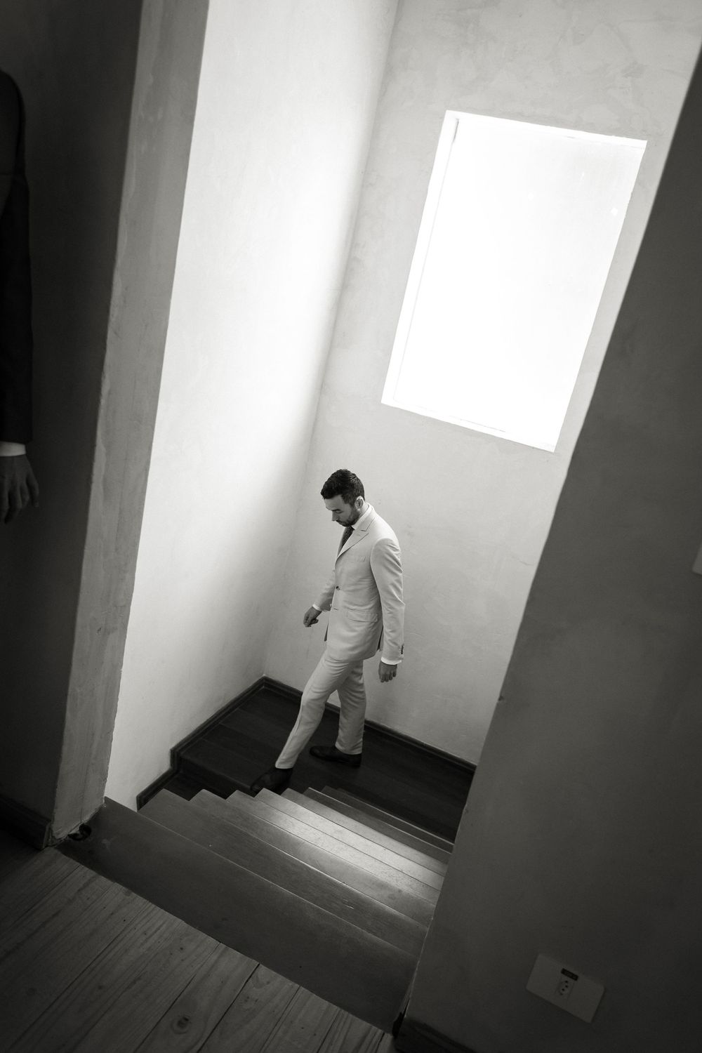 A person in a light colored suit descends a modern staircase with dramatic lighting from above.