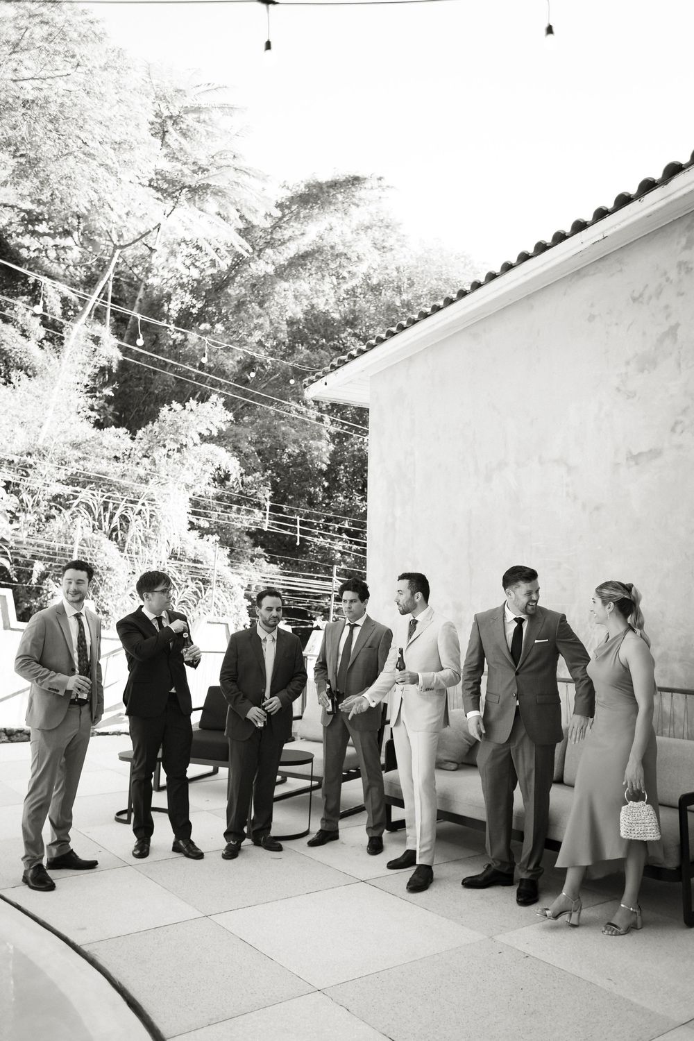 Wedding guests line up against a white wall outdoors during a formal event.