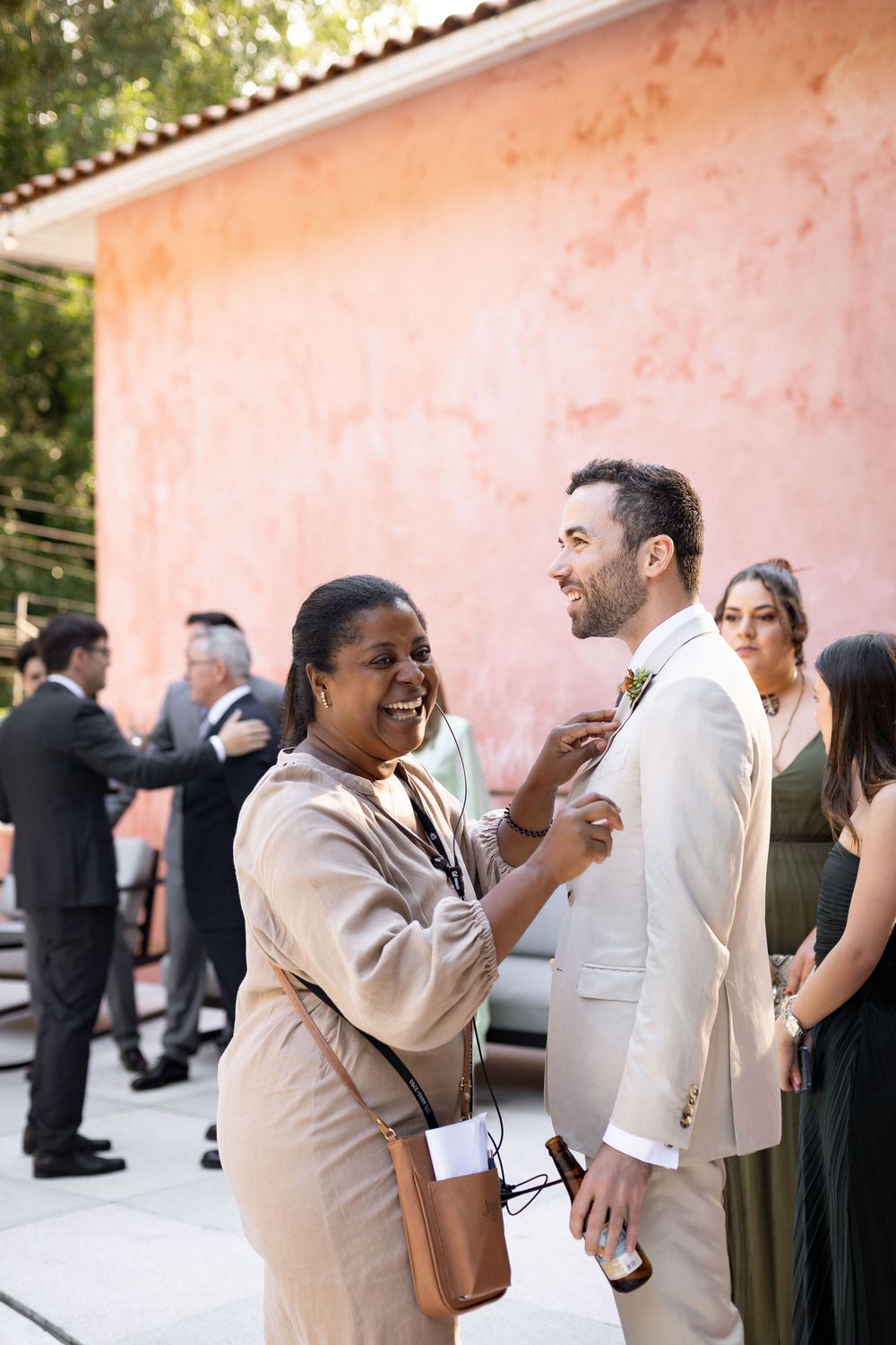 Wedding guests sharing a joyful moment at an outdoor reception against a pink stucco wall.