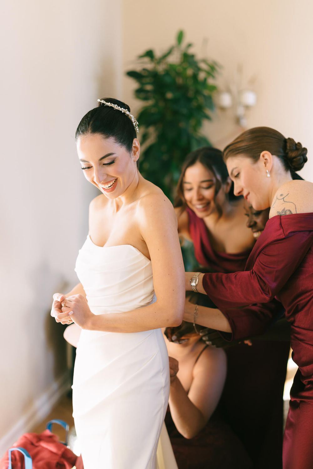 Bridesmaids in burgundy dresses help the bride prepare on her wedding day.