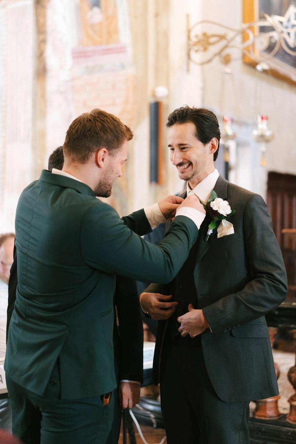 Groomsmen in dark suits share lighthearted moments and laughter during formal wedding photos.