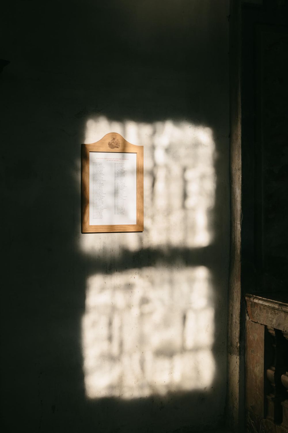 Sunlight casts geometric window shadows on dark interior walls in a moody architectural series.