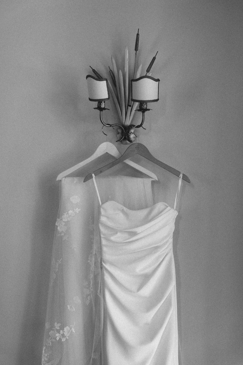 A white wedding dress hangs elegantly on a display stand in a soft, dreamy black and white photograph.