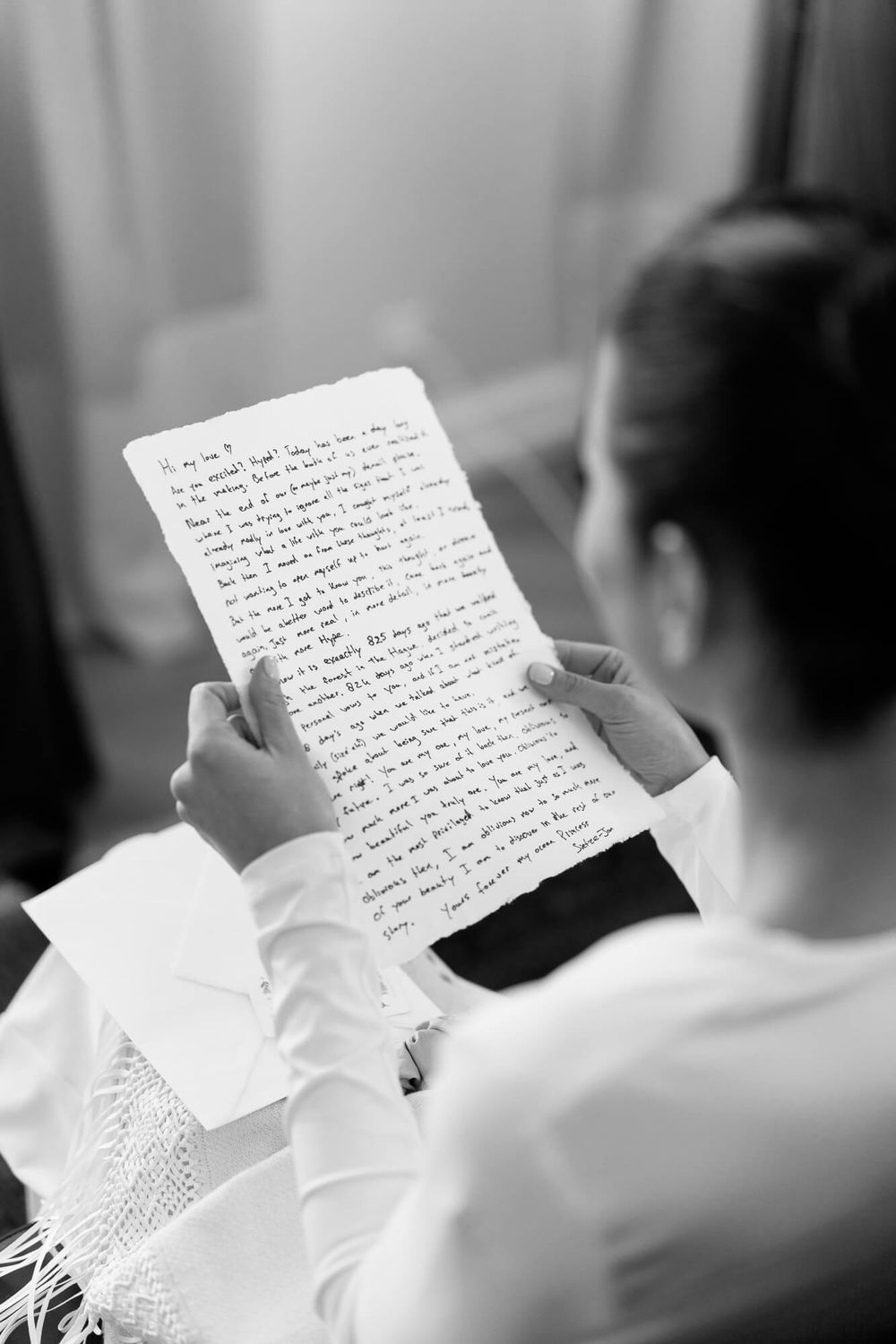 A person in white clothing reads a handwritten letter in a candid black and white photograph.