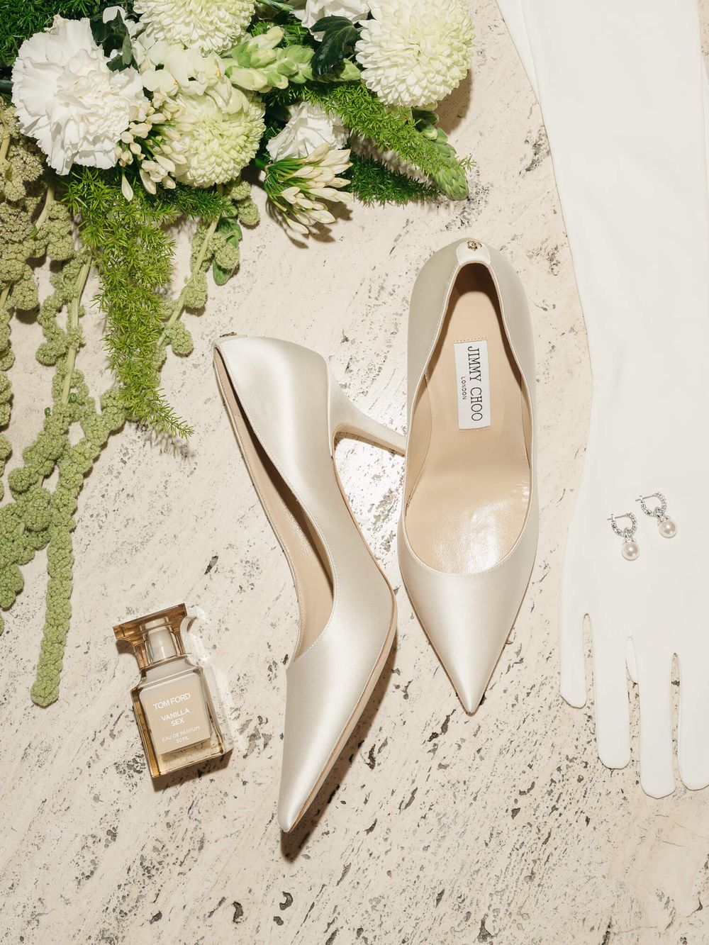 Elegant ivory bridal heels with floral bouquets arranged on a textured cream background.
