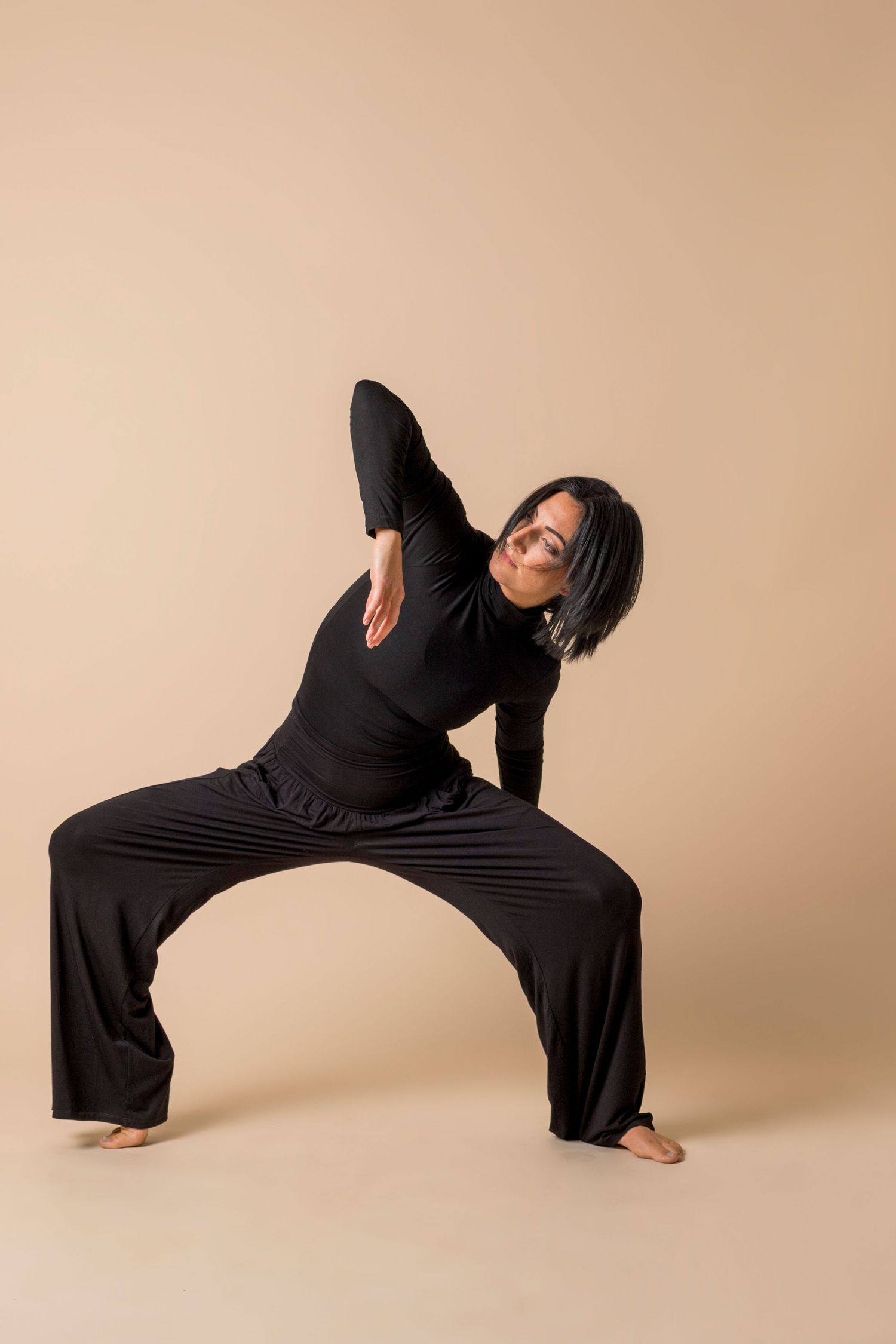 A dancer in black clothing performs a series of fluid stretching movements against a beige backdrop.