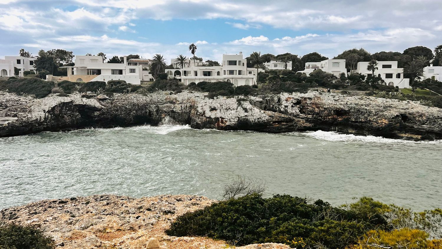 A coastal town with white buildings nestled among rocky cliffs and surrounded by a turquoise sea.