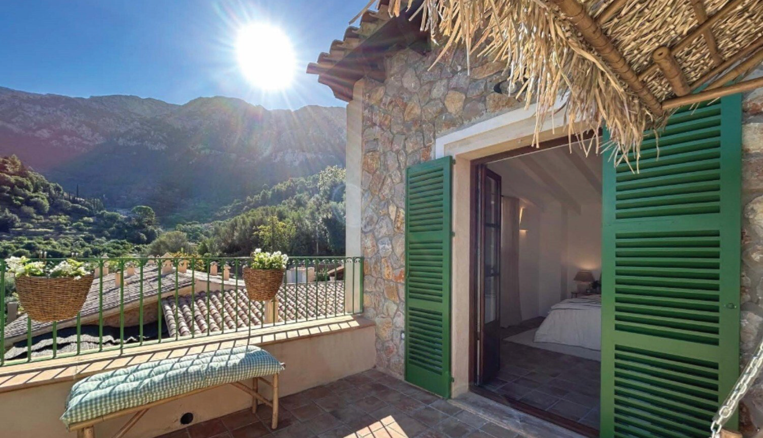 Mediterranean mountain village balcony with green shutters and panoramic views of sunlit hillsides and stone buildings.