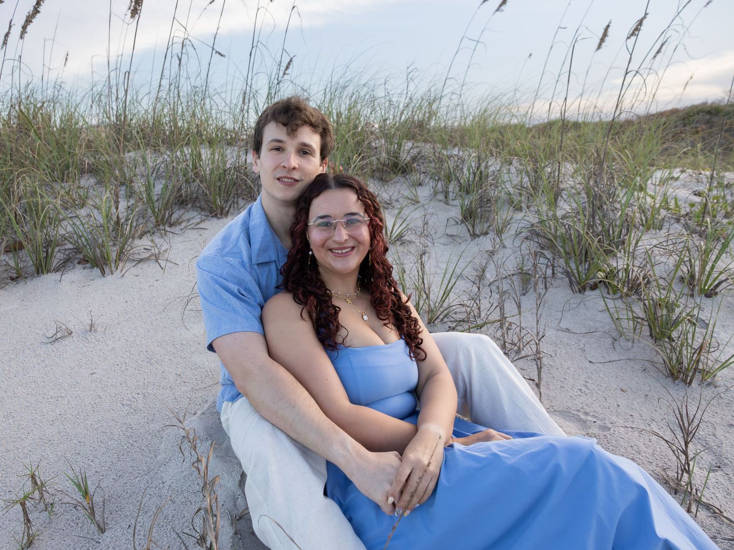 Young couple sitting together on white sand dunes surrounded by sea grass at twilight.