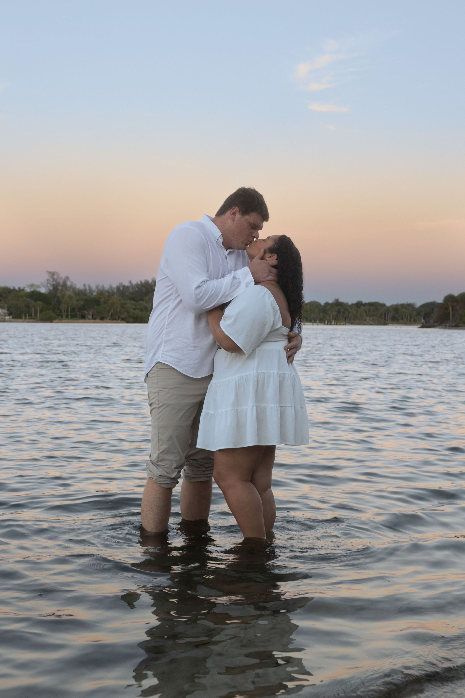 Couple kissing while standing in calm lake water at golden hour sunset.