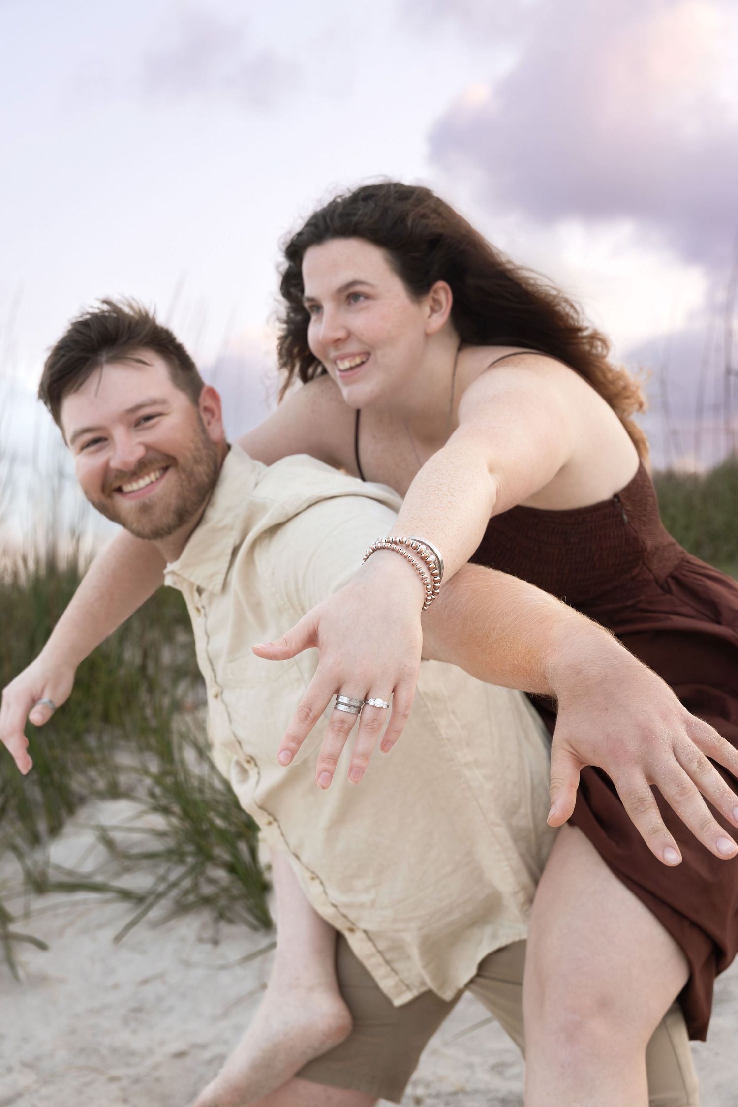 Man giving woman a piggyback ride on sandy beach dunes at sunset.