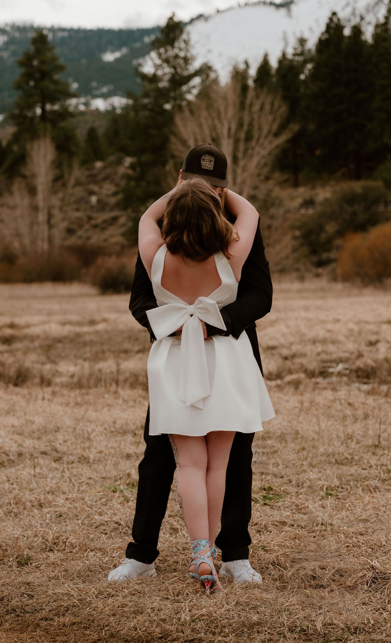 A couple in contrasting black and white outfits poses intimately in a rustic outdoor field setting.