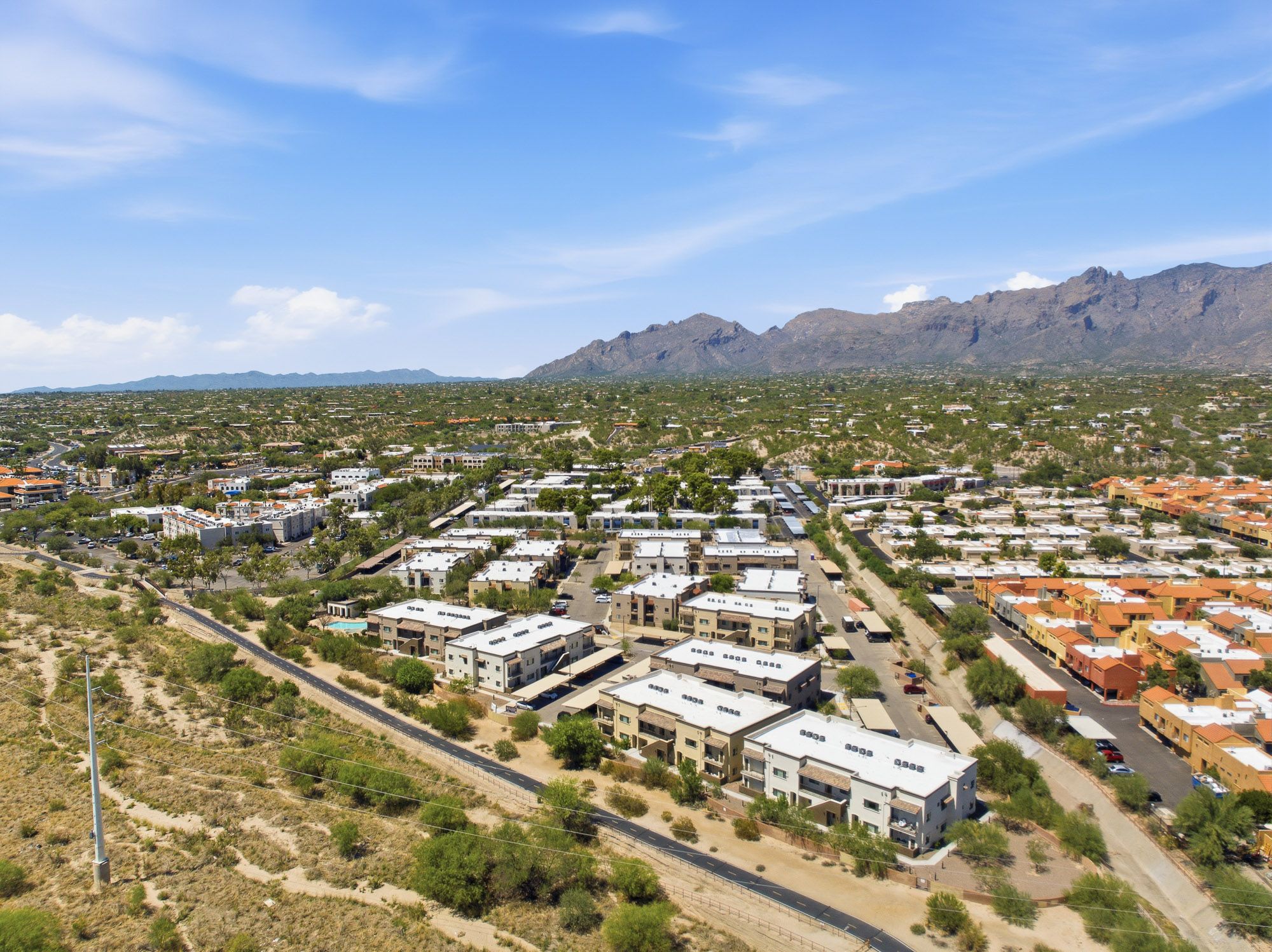 Aerial view of a residential neighborhood with modern apartments surrounded by desert landscape and mountains.