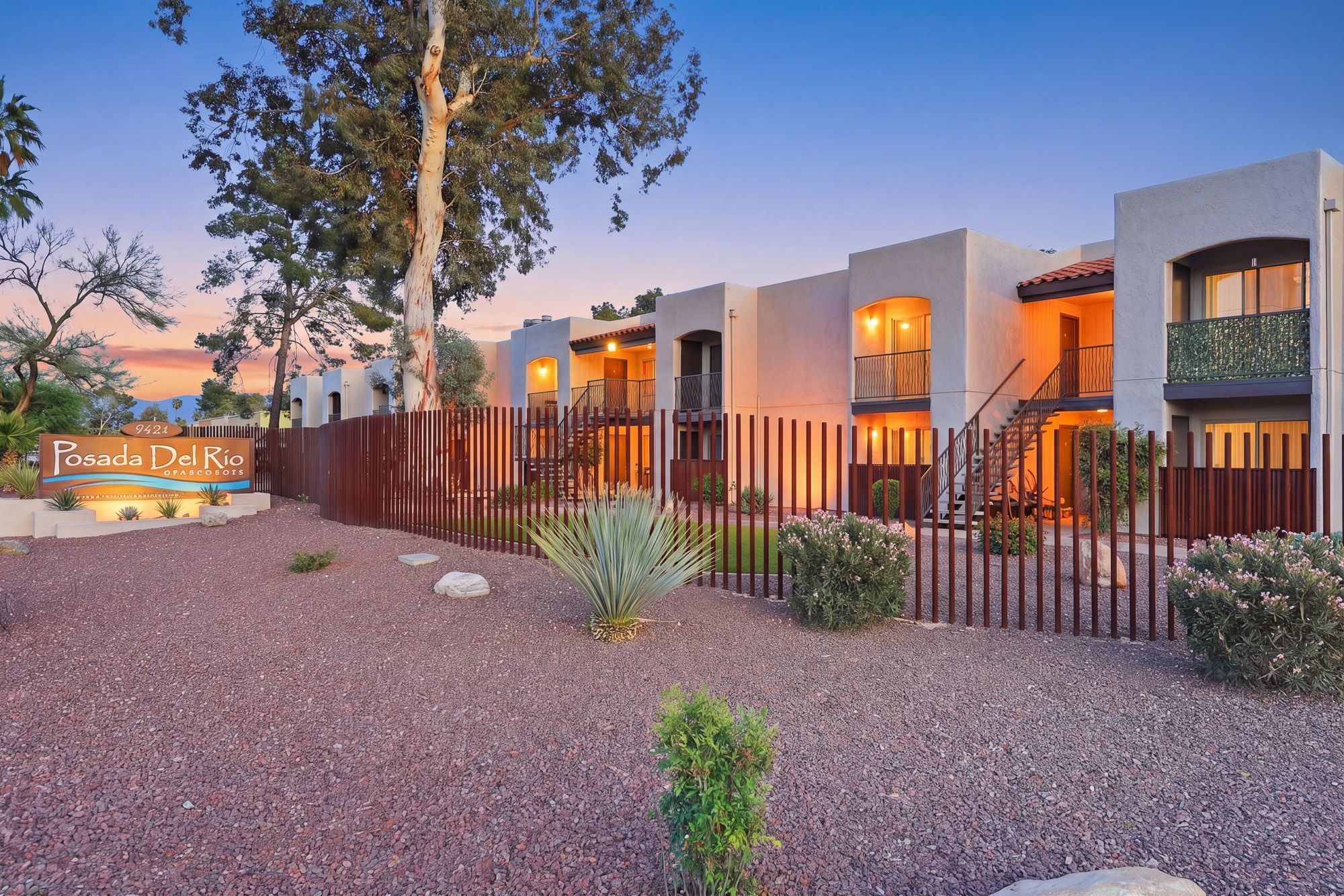 Southwest-style townhomes at dusk with desert landscaping, agave plants, and warm glowing windows at Posada Del Rey.