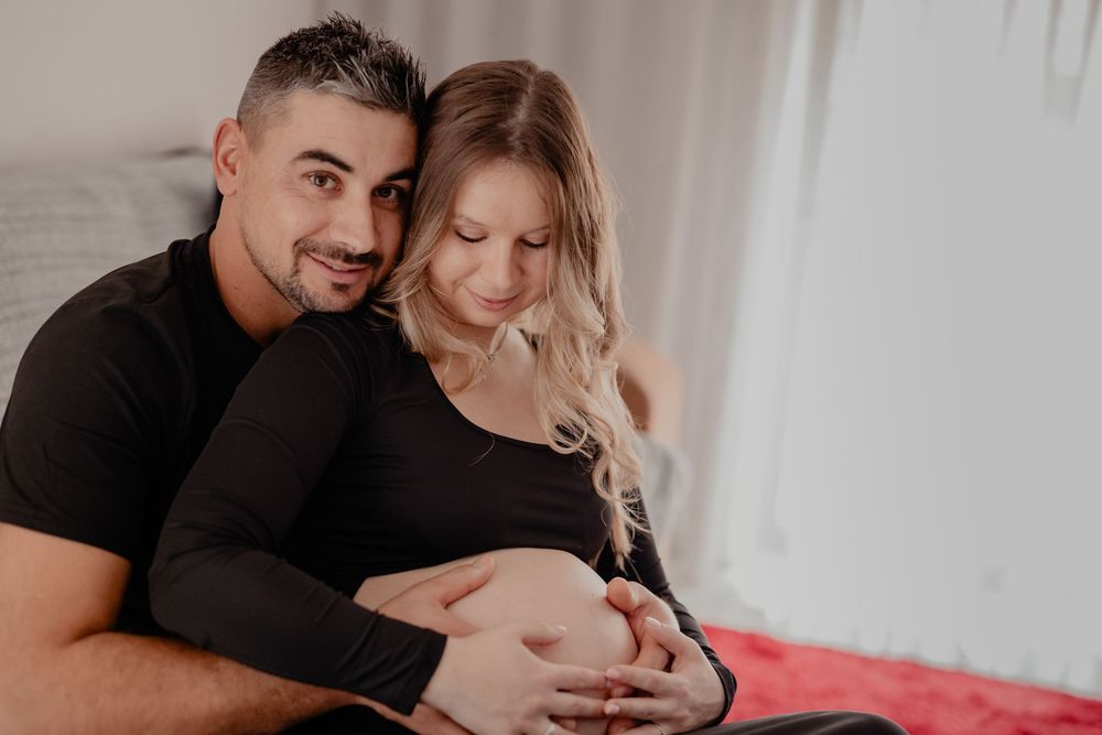 Expecting couple shares tender moments during maternity photo shoot in bright white room.