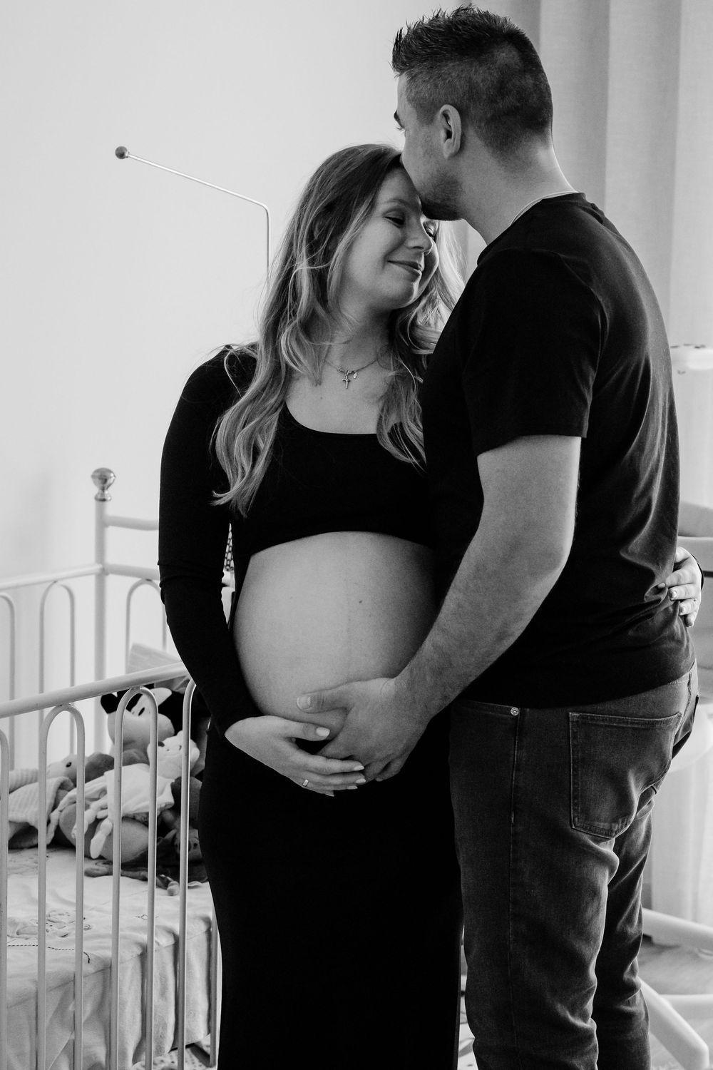 Expecting couple shares intimate black and white maternity photos in front of a white crib.