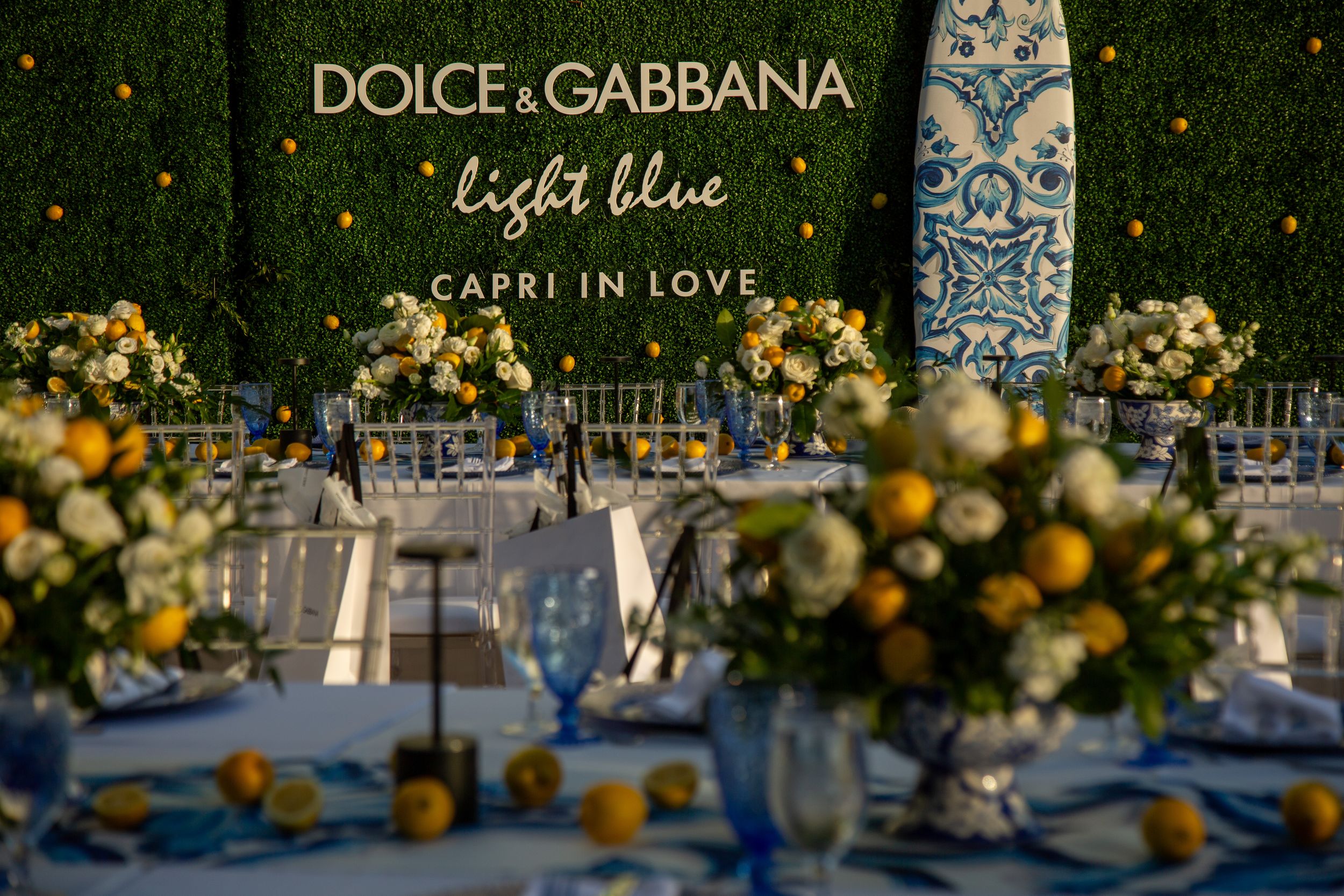 Elegant wedding reception table setting with floral arrangements and Dolce & Gabbana branding against a dark background.