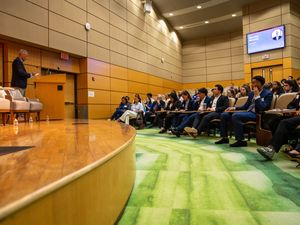 Students seated in a modern lecture hall listen attentively to a speaker presenting at a podium.