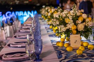 Elegant banquet table with blue glassware, white roses, and lemons at a Dolce & Gabbana event.