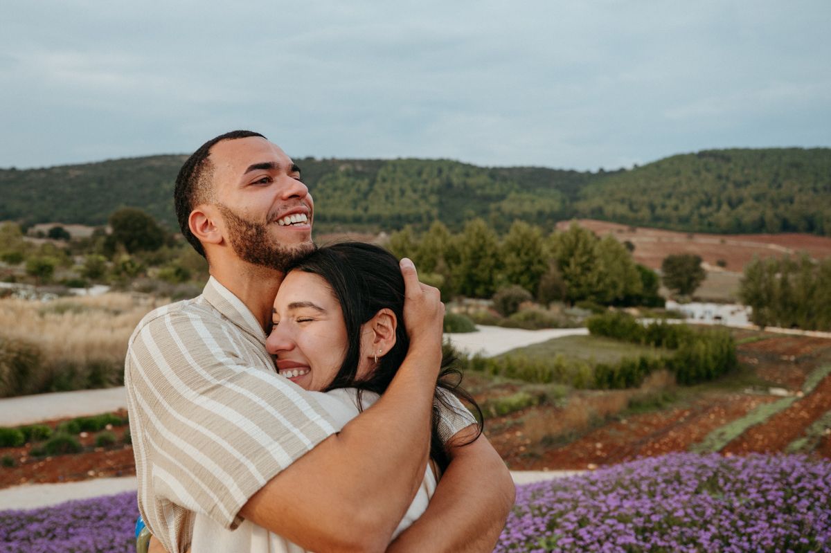 A couple embraces in a lavender field during sunset with mountains in the background.