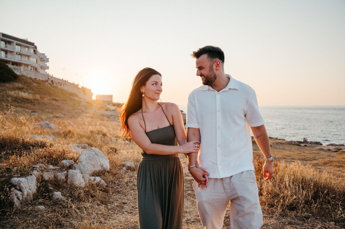 Couple sharing romantic moments along a scenic coastal cliff during golden hour sunset.