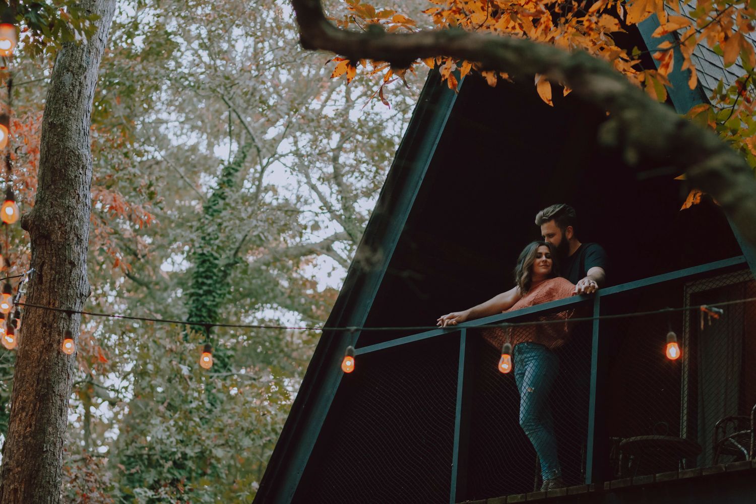 couple stand on the balcony of their a-frame B&B, surrounded by patio lanterns, 1000 islands ontario