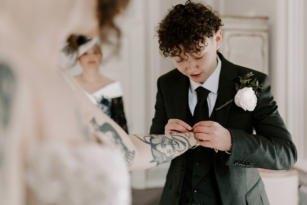 Groomsmen in black suits help each other prepare by adjusting ties and boutonnieres before wedding ceremony.